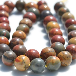 Puede incluir: Una hebra de cuentas de piedras preciosas multicolores. Las cuentas son redondas y tienen un aspecto moteado con tonos de marr&oacute;n, rojo y gris. Las cuentas est&aacute;n enhebradas en un cord&oacute;n transparente.