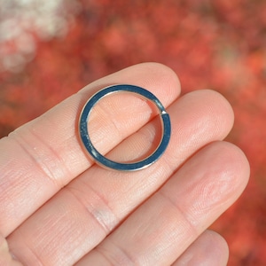 May include: A shiny, silver-colored key ring. The circular ring is held in a hand against a blurred background of red and orange hues. The key ring is made of metal.