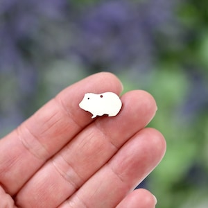 May include: White metal charm shaped like a guinea pig. The charm is small and has a hole for attaching to a necklace or bracelet.