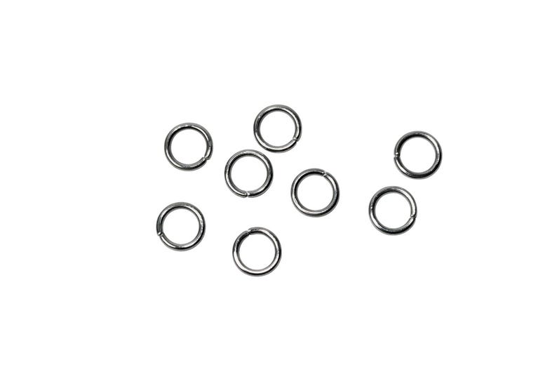 May include: A collection of seven small, circular silver-toned metal jump rings. Each ring features a single thin opening along its circumference, designed for connecting jewelry components. The rings are arranged in a loose, scattered formation.