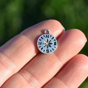 May include: Silver compass charm with a star design and the letters N, E, S, and W around the edge.
