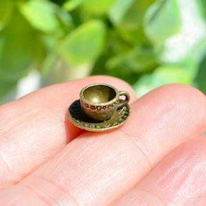May include: A miniature bronze teacup and saucer set. The cup has a handle and the saucer has a decorative edge.