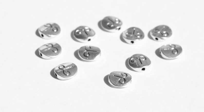 May include: A collection of silver metal beads with a symbol of a ram's head on each bead.