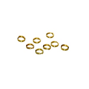 May include: A group of ten gold jump rings, scattered on a white background.