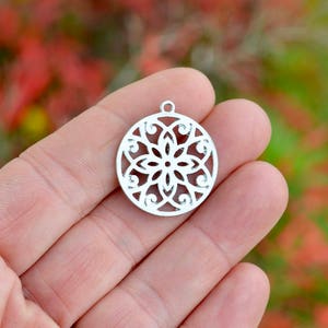 May include: Silver pendant with a circular, intricate, cut-out design resembling a flower.