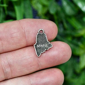 May include: Silver charm shaped like the state of Maine with the word "MAINE" inscribed on it.