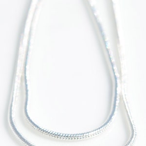 Puede incluir: Un collar de cadena de serpiente de plata. La cadena est&aacute; hecha de peque&ntilde;os eslabones entrelazados que crean un aspecto liso y fluido.