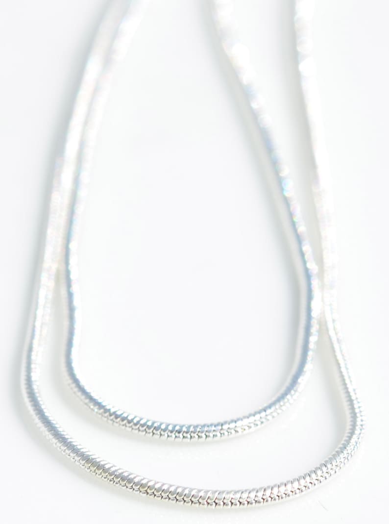 Puede incluir: Un collar de cadena de serpiente de plata. La cadena est&aacute; hecha de peque&ntilde;os eslabones entrelazados que crean un aspecto liso y fluido.