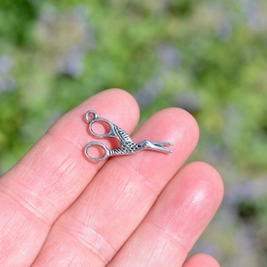 May include: Silver-toned metal charm shaped like a pair of scissors with a bird design.