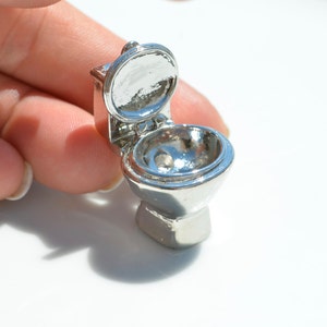 May include: A miniature silver toilet with the lid open. The toilet is made of metal and has a shiny finish.