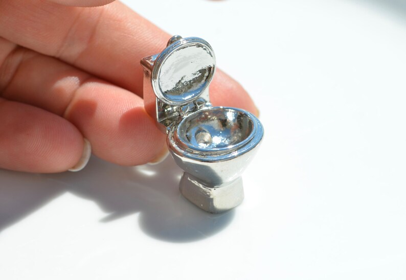 May include: A miniature silver toilet with the lid open. The toilet is made of metal and has a shiny finish.