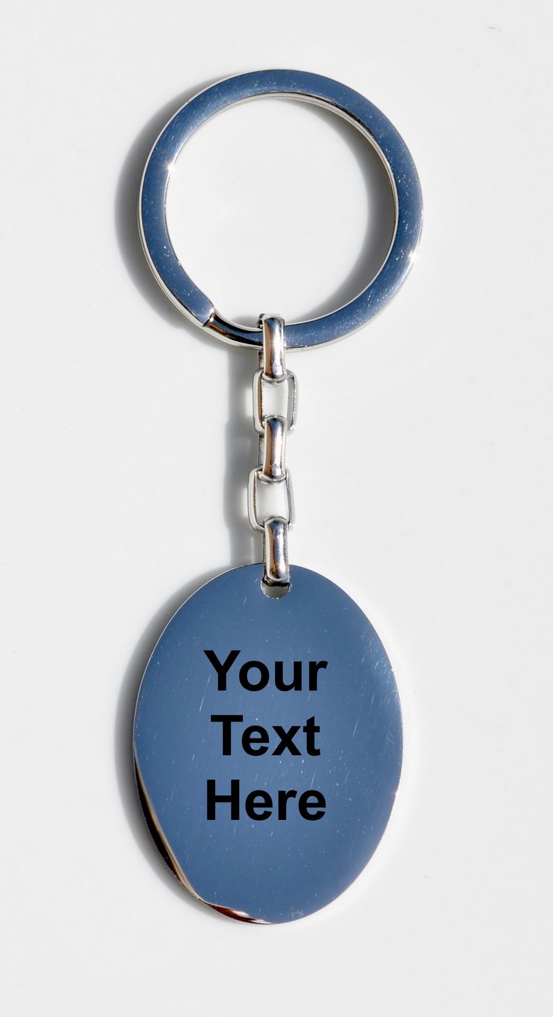 Puede incluir: Llavero plateado con un colgante ovalado. El colgante tiene el texto "Your Text Here" en negro. El llavero incluye un anillo y un eslab&oacute;n de cadena. El fondo es blanco.