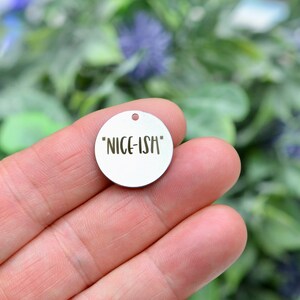 May include: A silver round charm with the text "NICE-ISH" engraved on it.