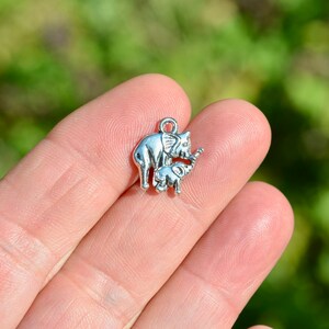 May include: Silver charm featuring a mother elephant and her baby elephant. The charm is perfect for adding a touch of whimsy to jewelry or crafts.