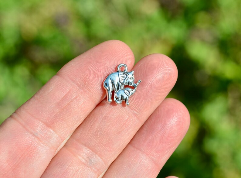 May include: Silver charm featuring a mother elephant and her baby elephant. The charm is perfect for adding a touch of whimsy to jewelry or crafts.