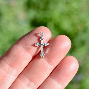 May include: A silver cross charm with a detailed design. The cross is small and delicate, perfect for adding a touch of faith to jewelry or crafts.