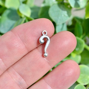 May include: Silver question mark charm pendant. The charm is small and has a simple design.