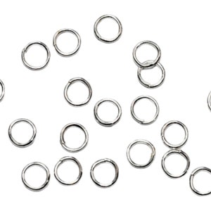 May include: A scattering of silver jump rings, a type of jewelry finding, on a white background.