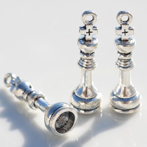 May include: Three silver chess piece charms, two kings and one pawn. The kings have a cross on top and the pawn has a round top.