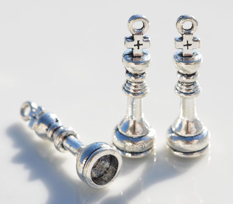 May include: Three silver chess piece charms, two kings and one pawn. The kings have a cross on top and the pawn has a round top.