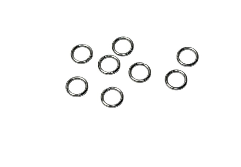 Op de afbeelding: Een verzameling van zeven kleine, ronde zilverkleurige metalen buigringen. Elke ring heeft een dunne draadconstructie met een zichtbare opening, ontworpen voor het verbinden van sieradenonderdelen. De ringen zijn in een verspreid patroon gelegd.
