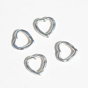 May include: Four silver heart-shaped charms with an open center. The charms are on a white background.