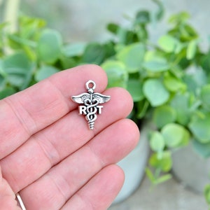 May include: Silver charm with a medical caduceus symbol and the letters "R.O.T." on it.