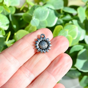 May include: Silver sunflower charm with a detailed design. The charm is small and perfect for adding a touch of nature to jewelry or crafts.
