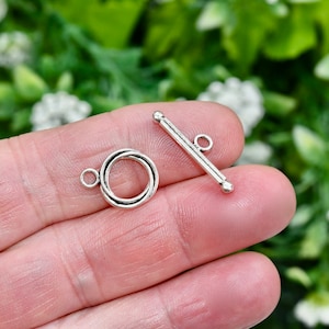 May include: Silver tone toggle clasp with a round ring and a bar with a loop. The clasp is used for necklaces, bracelets, and other jewelry.