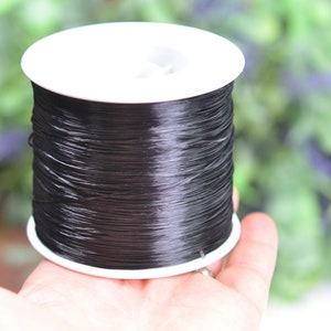 May include: A spool of black elastic cord, wound tightly on a white plastic bobbin.