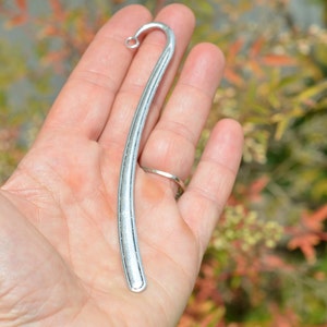 May include: A silver bookmark with a curved shape and a smooth, polished finish.