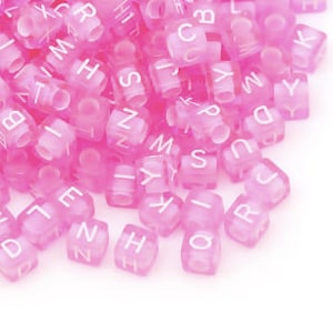 May include: A pile of pink alphabet letter beads. The letters are in white and are visible on the pink beads.