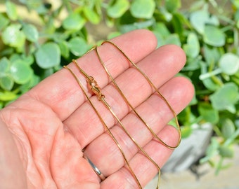 May include: A gold chain necklace with a lobster clasp. The chain is thin and delicate, and it is lying on a hand.
