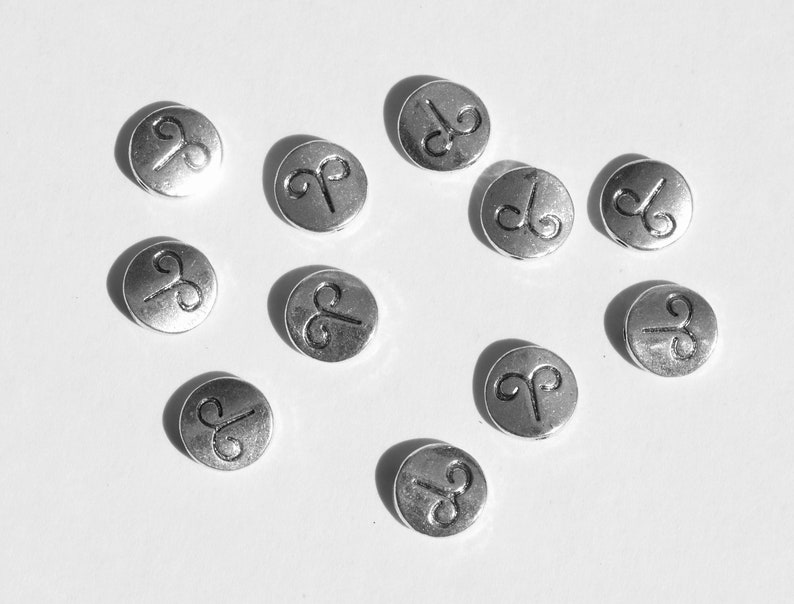 May include: Ten silver-colored metal beads with a raised Aries zodiac symbol on each bead.