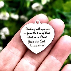 May include: A silver-toned heart-shaped metal pendant featuring an engraved inscription that reads: Nothing will separate us from the love of God, which is in Christ Jesus our Lord. Romans 8:38-39. The charm includes a small loop at the top.