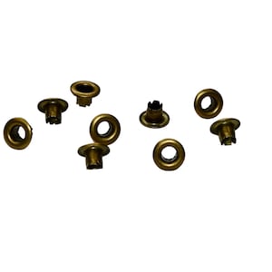 May include: A group of ten gold-colored metal eyelets, scattered on a white background.