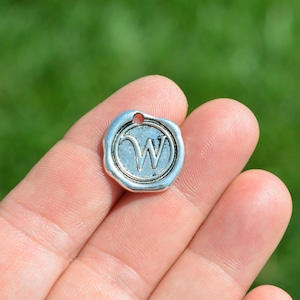 May include: Silver charm with a raised letter W in a wax seal design.