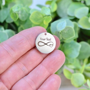 May include: Silver round charm with an infinity symbol and a small heart. The charm has the text "Your Text" engraved on it.