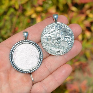May include: Two silver-toned pendant charms, one with a detailed design of a vintage steam train and the other with a blank circular space for adding a photo or design.