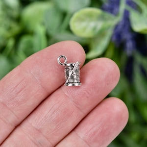 May include: Silver charm in the shape of a spool of thread with a needle sticking out of it.