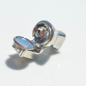 May include: A silver-colored miniature toilet charm with the lid open. The charm is small enough to fit on a keychain or bracelet.