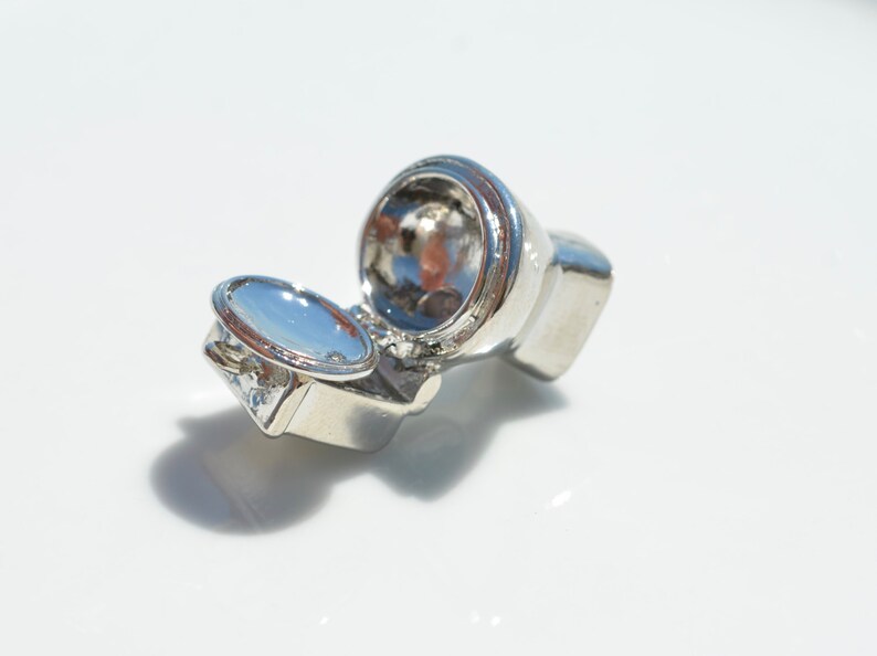 May include: A silver-colored miniature toilet charm with the lid open. The charm is small enough to fit on a keychain or bracelet.
