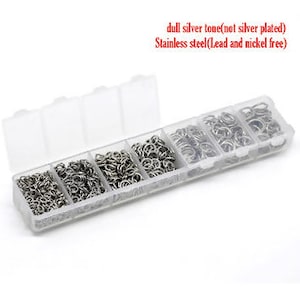May include: A clear plastic container with six compartments filled with silver jump rings. The container is labeled "dull silver tone (not silver plated) Stainless steel (Lead and nickel free)".
