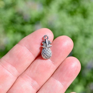 May include: Silver pineapple charm with a detailed design. The charm is small and would be perfect for adding to jewellery or crafts.