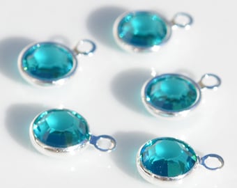 May include: Five turquoise blue crystal charms with silver settings and jump rings. The charms are round and have a faceted design.