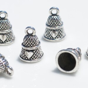 Peut inclure: Un ensemble de six breloques en forme de d&eacute; &agrave; coudre en m&eacute;tal argent&eacute;, chacune pr&eacute;sentant un motif textur&eacute; en croisillons et un petit c&oelig;ur en relief sur le c&ocirc;t&eacute;. Chaque breloque comporte une boucle circulaire sur le dessus.