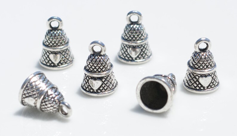 Peut inclure: Un ensemble de six breloques en forme de d&eacute; &agrave; coudre en m&eacute;tal argent&eacute;, chacune pr&eacute;sentant un motif textur&eacute; en croisillons et un petit c&oelig;ur en relief sur le c&ocirc;t&eacute;. Chaque breloque comporte une boucle circulaire sur le dessus.