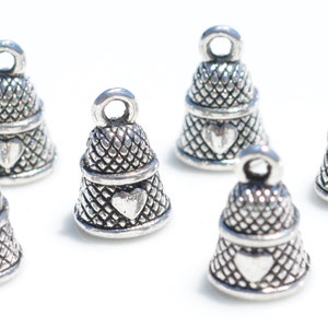 Peut inclure: Six breloques en m&eacute;tal argent&eacute; en forme de d&eacute;s &agrave; coudre, chacune pr&eacute;sentant un motif quadrill&eacute; textur&eacute; sur la partie sup&eacute;rieure et un embl&egrave;me en forme de c&oelig;ur lisse et en relief sur la partie inf&eacute;rieure, surmont&eacute;es d'une petite boucle.