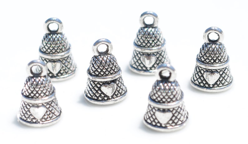 Peut inclure: Six breloques en m&eacute;tal argent&eacute; en forme de d&eacute;s &agrave; coudre, chacune pr&eacute;sentant un motif quadrill&eacute; textur&eacute; sur la partie sup&eacute;rieure et un embl&egrave;me en forme de c&oelig;ur lisse et en relief sur la partie inf&eacute;rieure, surmont&eacute;es d'une petite boucle.