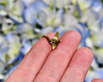 May include: A small gold origami crane figurine held in a hand. The crane is a traditional Japanese symbol of peace and good luck.